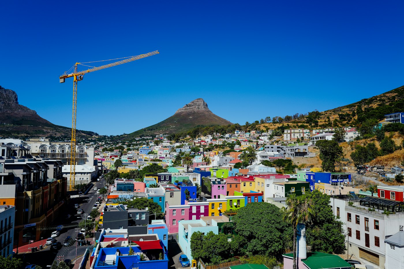 Colourful Bo-Kaap houses beside a construction crane, with Lion's Head behind